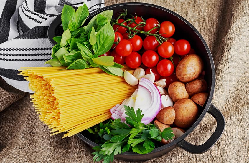 bir tencerenin içerisinde spaghetti makarna, maydanoz, nane, soğan, sarımsak, domates ve patates yer almaktadır.